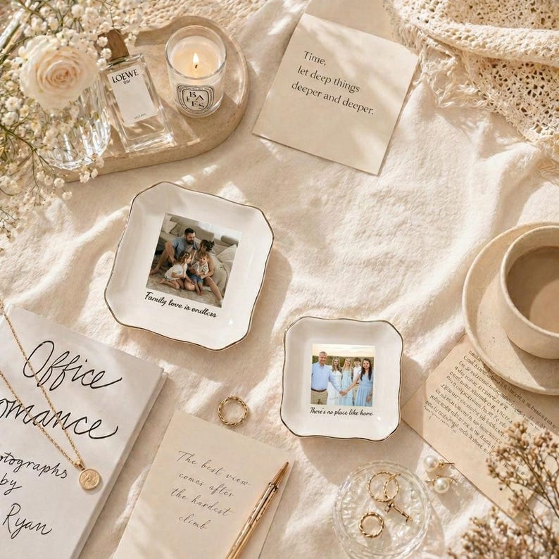 Puede incluir: Una variedad de elementos decorativos dispuestos sobre una superficie color crema. Incluye dos platos cuadrados con fotos familiares, un frasco de perfume, una vela encendida, una taza de caf&eacute;, joyas y notas manuscritas con texto. El texto en los platos dice "Family love is endless" y "There's no place like home."
