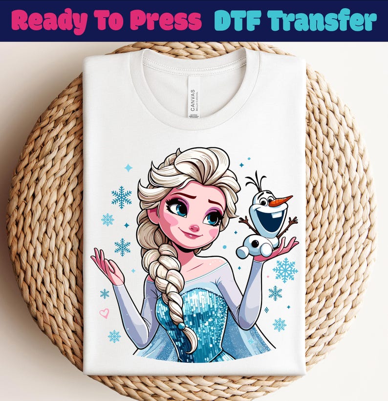 May include: White t-shirt with a cartoon image of Elsa and Olaf from Frozen, surrounded by snowflakes. The text "Ready To Press DTF Transfer" is at the top. The shirt is folded on a woven surface.