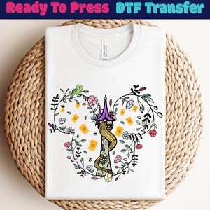Peut inclure: T-shirt blanc avec un graphisme coloré d'une tour, de fleurs et de lanternes flottantes, entouré d'une couronne florale. Le texte "Ready To Press DTF Transfer" est en haut.