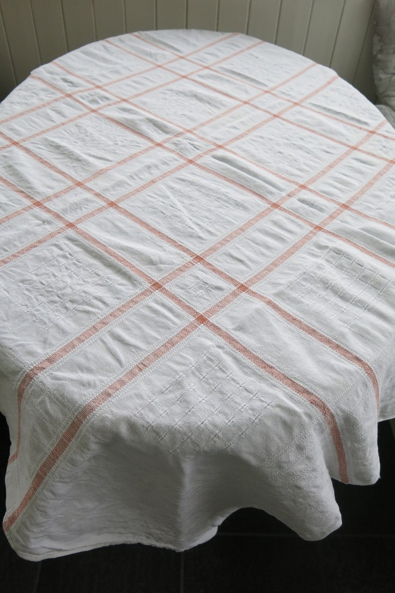 K&ouml;nnte beinhalten: Wei&szlig;e Tischdecke mit rosafarbenem Karomuster. Die Tischdecke ist rund und hat einen leicht gewellten Rand.