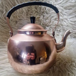 以下が含まれることがあります： 黒いハンドルと蓋が付いた銅色のティーケトル。 ケトルは丸みを帯びたボディと湾曲した注ぎ口を備えています。 ハンドルは黒い素材で包まれています。 ケトルはおそらく銅または銅合金で作られています。