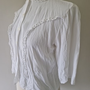 Könnte beinhalten: Weiße Bluse mit Knöpfen, hohem Kragen und Spitzenbesatz. Die Spitze befindet sich am Kragen, an der Vorderseite der Bluse und an den Ärmeln.