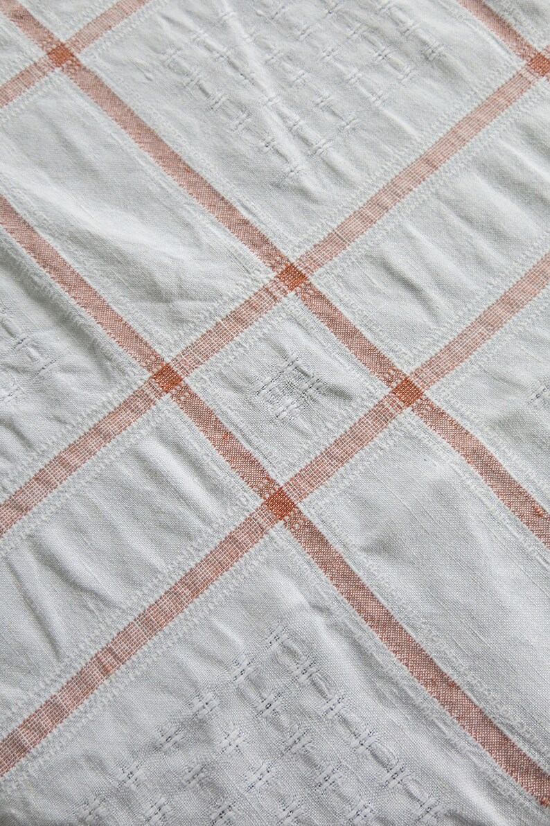 K&ouml;nnte beinhalten: Wei&szlig;er Tischdeckenstoff mit einem karierten Muster in hellorange.