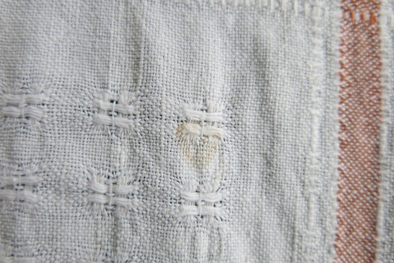 K&ouml;nnte beinhalten: Nahaufnahme eines wei&szlig;en gewebten Stoffes mit einem kleinen braunen Fleck. Der Stoff hat ein strukturiertes Muster und einen braunen Rand.