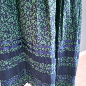 May include: A long, dark blue skirt with a green and white floral pattern. The skirt has a black lace trim and blue ribbon accents.