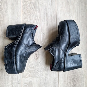 Puede incluir: Par de botas de plataforma negras con un diseño de inspiración western. Las botas tienen una suela de plataforma gruesa y un tacón de bloque. La parte superior presenta costuras decorativas y una puntera puntiaguda. El forro interior es rojo.