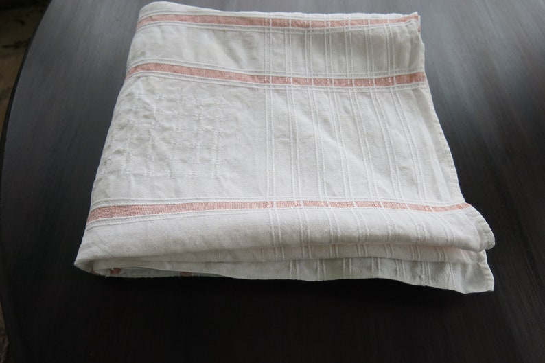 K&ouml;nnte beinhalten: Eine wei&szlig;e Leinen-Tischdecke mit rosa Streifen. Die Tischdecke ist gefaltet und hat ein zartes Stickmuster.