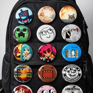 May include: A black backpack covered in colorful pinback buttons. The buttons feature various designs, including cartoon characters, anime figures, and text like "Netflix Series" and "Fazbear Entertainment".