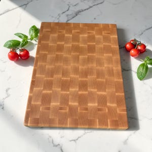 Flat lay of the maple end grain cutting board on marble, styled with cherry tomatoes on the vine and fresh basil leaves on either side.