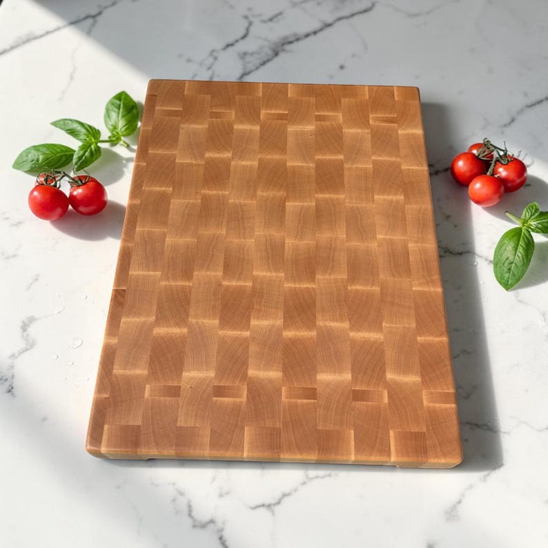 Flat lay of the maple end grain cutting board on marble, styled with cherry tomatoes on the vine and fresh basil leaves on either side.