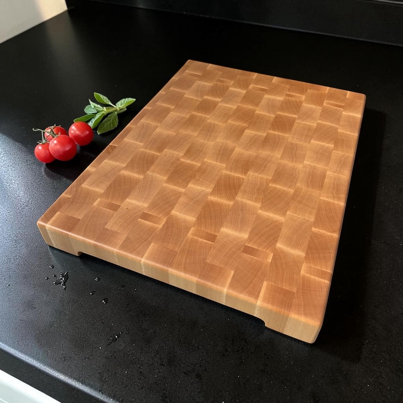 Handcrafted maple end grain cutting board with hand grip cutout, cherry tomatoes and basil at its side