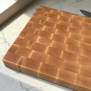Close-up angled view of the end grain maple butcher block, showing the checkerboard grain pattern and its thick edge on a marble surface.