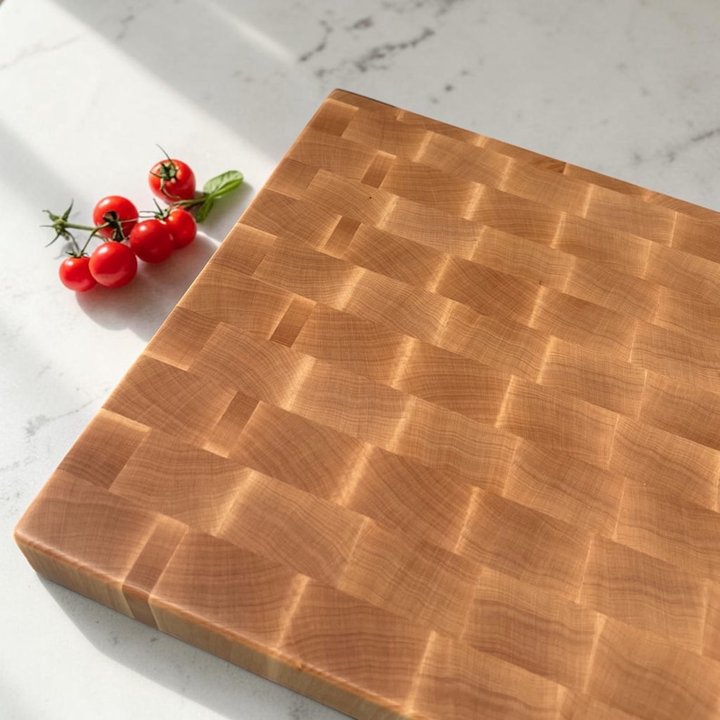 Overhead angled view of the maple end grain chopping block showing its full checkerboard surface, with cherry tomatoes on the vine to the side on marble.