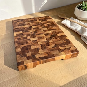 Handmade walnut end grain cutting board on kitchen table, thick butcher block chopping board made from natural walnut wood, premium wooden cutting board for kitchen, durable chef board for cutting meat, vegetables and food preparation