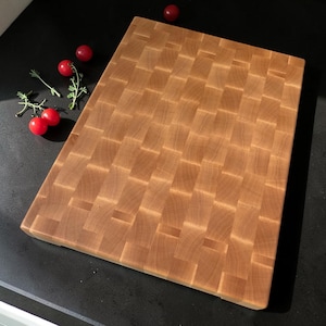 Maple end grain chopping board lying diagonally on a dark counter with cherry tomatoes on the vine