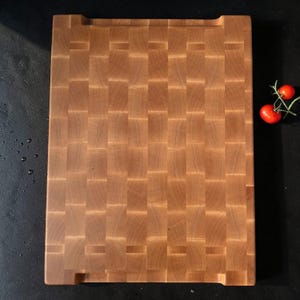 Top-down view of the maple end grain butcher block with grip cutouts on both ends and cherry tomatoes beside it