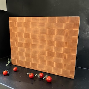 Maple end grain cutting board standing upright against a dark background with cherry tomatoes at its base