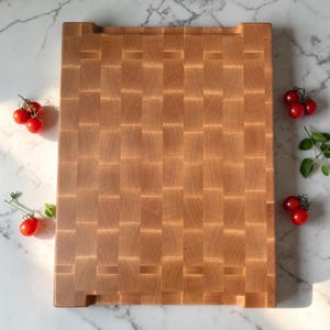 Overhead flat lay of the maple end grain cutting board on marble, framed by clusters of cherry tomatoes and fresh basil on every side.