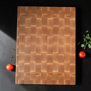 Overhead view of the flat maple end grain cutting board on a black surface with cherry tomatoes and greens beside it