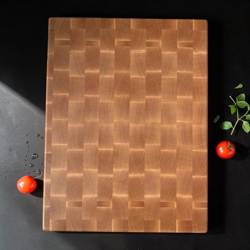 Overhead view of the flat maple end grain cutting board on a black surface with cherry tomatoes and greens beside it