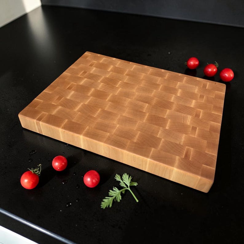 May include: A rectangular wooden cutting board featuring a woven basket-weave pattern made of light brown wood blocks. The board is positioned with several small red cherry tomatoes and a small green herb sprig placed around it.