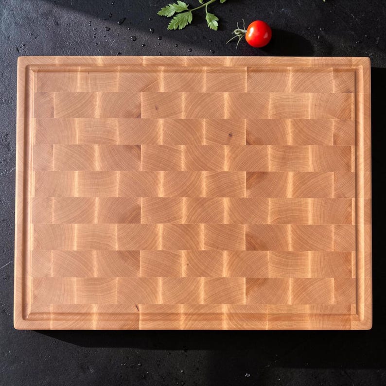 Maple end grain cutting board with juice groove, top view on a dark countertop with a cherry tomato and fresh parsley