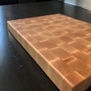 Maple end grain chopping block on a dark counter with water drops, showing the smooth oiled surface