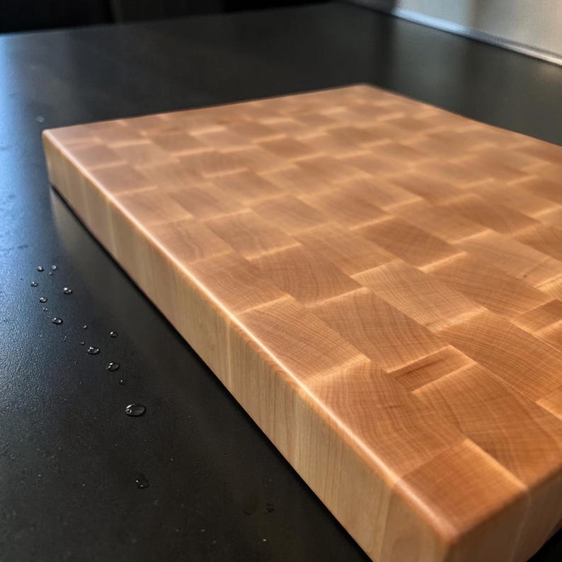 Maple end grain chopping block on a dark counter with water drops, showing the smooth oiled surface