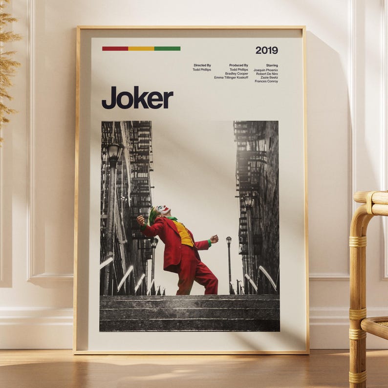 May include: A vertical poster featuring the 2019 film Joker. The design includes the title, production credits, and a black and white photograph of a person in a red suit and yellow vest dancing on stairs between buildings, framed in a light border.
