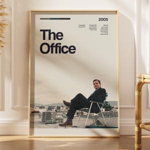 Könnte beinhalten: Ein vertikales Poster für die Fernsehserie The Office mit dem Titel in großer schwarzer Schrift, dem Jahr 2005 und Produktionsdaten. Das Bild zeigt eine Person im dunklen Anzug, die auf einem Klappstuhl auf einem Dach vor Stadtgebäuden sitzt.