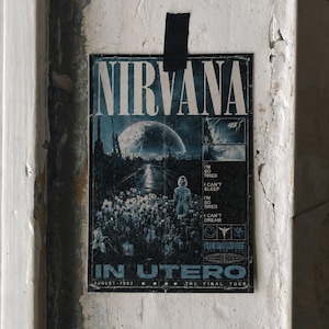 Peut inclure: Affiche vintage de Nirvana, avec le nom du groupe en lettres blanches au-dessus d'une image surréaliste d'une route, d'une lune et d'une silhouette. Le texte comprend "In Utero" et "August 1993". L'affiche est fixée à un mur blanc vieilli.