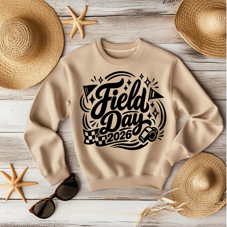 May include: A tan sweatshirt with the words "Field Day 2026" in black script and graphics. The sweatshirt is surrounded by straw hats, sunglasses, and starfish on a light wood background.