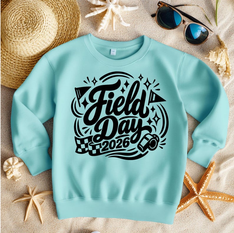 May include: A light blue sweatshirt with the words "Field Day 2026" in a black, stylized font. The design includes flags, stars, and a checkered flag. The sweatshirt is surrounded by a straw hat, sunglasses, starfish, and sand.