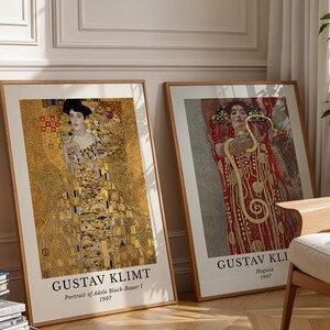 Peut inclure: Deux impressions d'art encadrées de Gustav Klimt. L'impression de gauche est Portrait of Adele Bloch-Bauer I, 1907, avec des motifs dorés. L'impression de droite est Hygieia, 1907, montrant une silhouette en rouge. Cadres en bois clair.