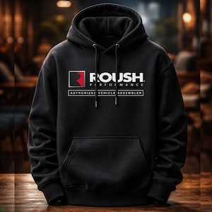 Pode incluir: Uma camisola com capuz preta com o logótipo Roush Performance em branco e vermelho no peito. O gráfico inclui o texto Roush Performance e Authorized Vehicle Assembler dentro de uma moldura retangular. Possui um bolso frontal tipo canguru.