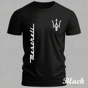 Può includere: T-shirt nera con logo Maserati bianco. Il design include il nome del marchio in verticale a sinistra e un'emblema del tridente sul petto destro. La parola "Black" è in basso a destra.