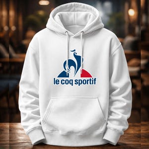 May include: White hoodie with a kangaroo pocket and a drawstring. The front displays a logo with a blue rooster, a red stripe, and the text "le coq sportif" in navy blue.