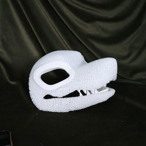 May include: A white, textured dragon mask with a large eye opening and detailed teeth. The mask is made of a porous material and is designed to be worn. The mask is a costume accessory.