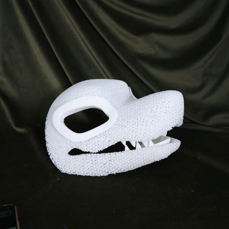May include: A white, textured dragon mask with a large eye opening and detailed teeth. The mask is made of a porous material and is designed to be worn. The mask is a costume accessory.