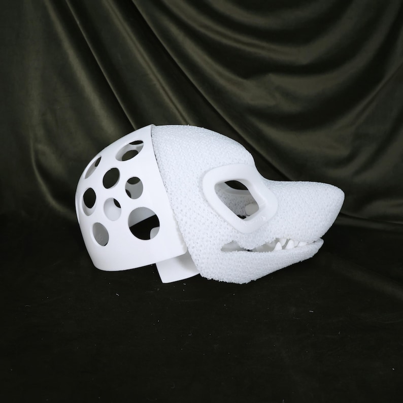 May include: A white, partially assembled fursuit head with a dog-like snout and open mouth. The head features a perforated section for ventilation and eye openings. The textured material contrasts with the smooth, solid white plastic.
