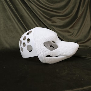 May include: A white, partially assembled fursuit head base. The base features a smooth, solid white section with circular cutouts and a textured, foam-like snout and face. The design includes eye and mouth openings.