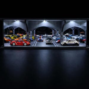 May include: A diorama featuring a collection of miniature car models in a parking garage setting. The scene is lit by overhead lights, highlighting the array of toy cars in various colours, including red, yellow, and white. The garage has concrete arches and parking space markings.
