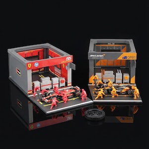 Puede incluir: Modelos en miniatura de coches de carreras de F&oacute;rmula 1 con escenarios de garaje. Un modelo presenta un coche rojo con el n&uacute;mero 55 y el nombre Carlos Sainz. El otro modelo presenta un coche negro y naranja con el logotipo de McLaren. Ambos modelos incluyen figuras en miniatura.