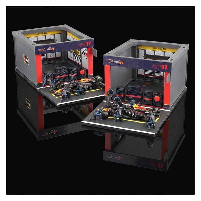 Puede incluir: Dos dioramas en miniatura de garaje de F&oacute;rmula 1. Cada uno presenta una estructura de garaje gris y roja con un coche de carreras, figuras en miniatura y herramientas. Los garajes est&aacute;n sobre una base negra, con el texto "SP11" visible en la parte superior.