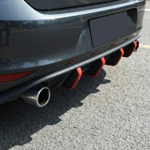 Può includere: Vista posteriore di un'auto grigio scuro con un tubo di scarico cromato e un paraurti nero con dettagli rossi. L'auto è parcheggiata su una superficie di asfalto grigia.