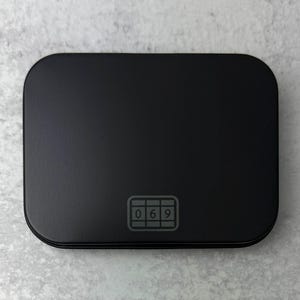 May include: A black rectangular box with a raised, rectangular, gray button that has the numbers 069 printed on it.