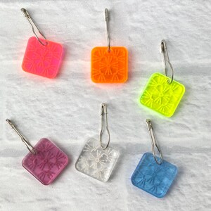 Pu&ograve; includere: Sei quadrati all'uncinetto colorati con spille di sicurezza argentate attaccate. I quadrati sono in tonalit&agrave; di rosa, arancio, giallo, bianco e blu.