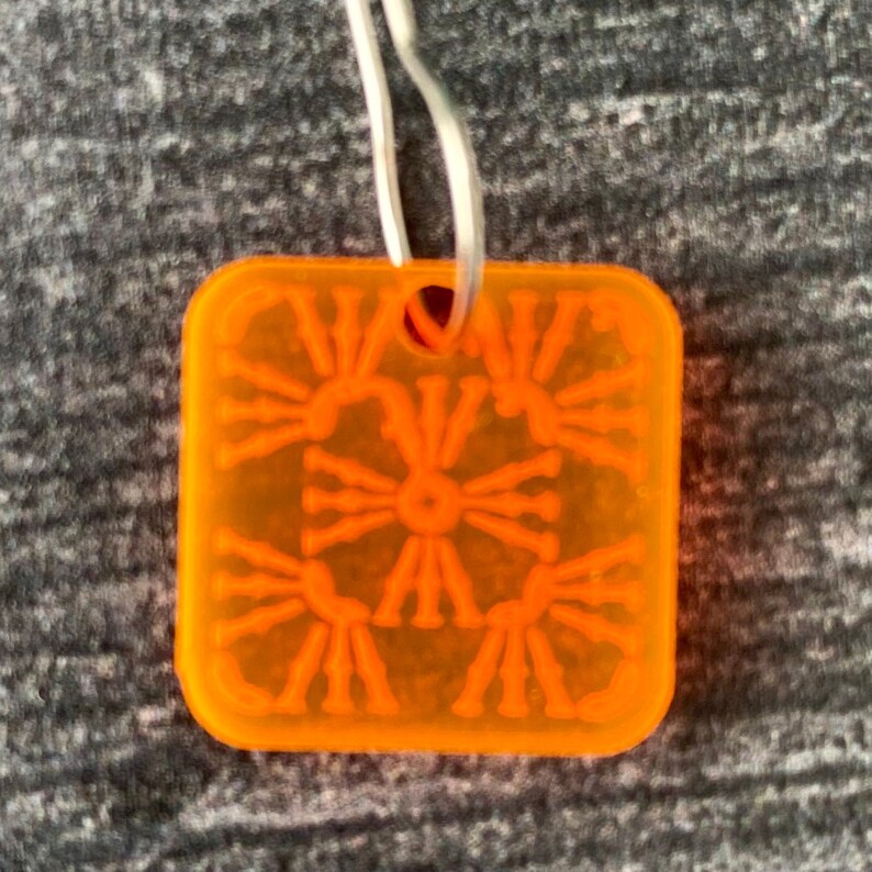 Pu&ograve; includere: Ciondolo in plastica arancione con un design geometrico. Il ciondolo ha un foro nella parte superiore per appenderlo.