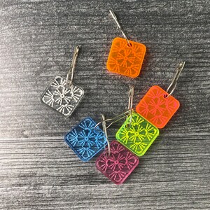 Pu&ograve; includere: Sei marcapunti a uncinetto in plastica colorata con anelli in metallo argentato. I marcapunti hanno la forma di quadrati e presentano diversi punti a uncinetto colorati.