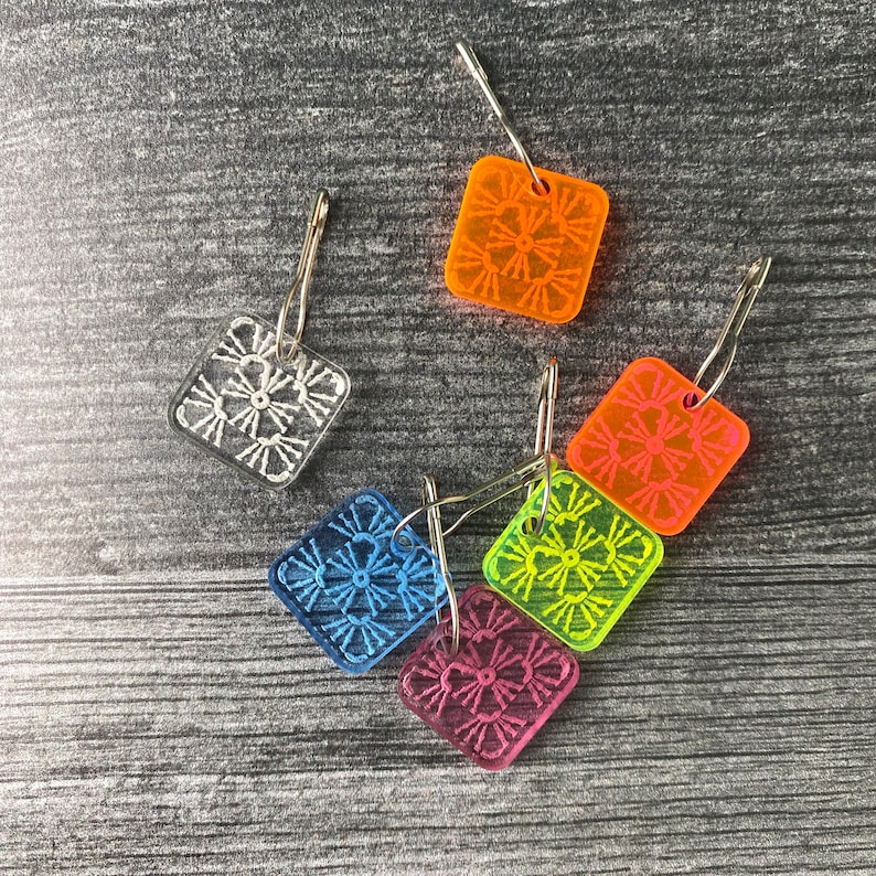 Pu&ograve; includere: Sei marcapunti a uncinetto in plastica colorata con anelli in metallo argentato. I marcapunti hanno la forma di quadrati e presentano diversi punti a uncinetto colorati.